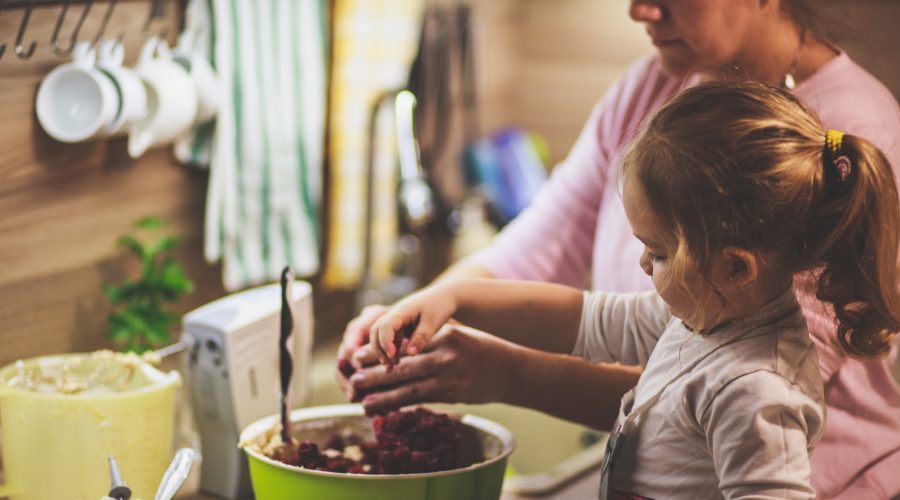 Little girl mixing cherries in the cake batter with her mother